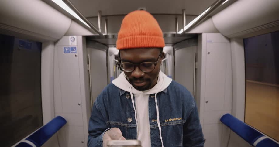 A man standing on a moving subway train holding his phone in one hand texting