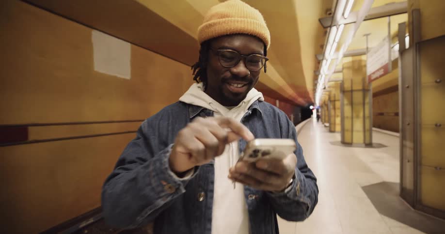 A man in a building smiles as he taps his cell phone