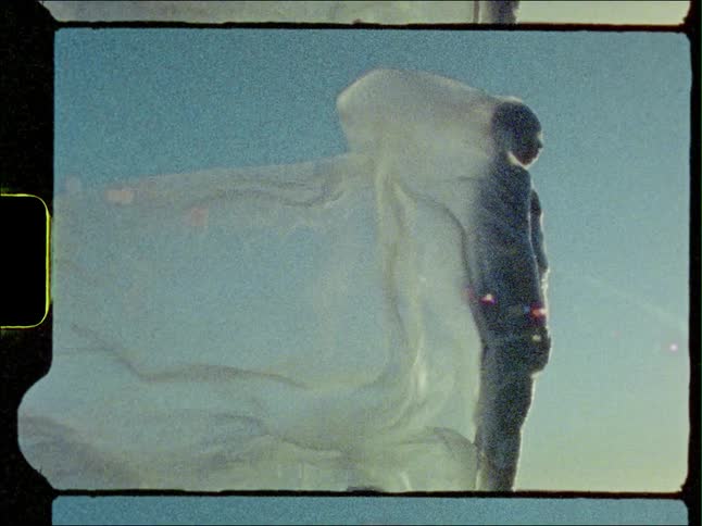 Wind blows through a white cloth draped over a man standing outside