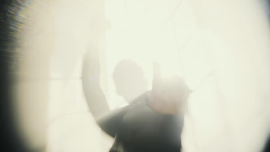 The sun shines brightly upon a man standing outside dancing with his arms in the air