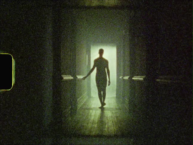 A man holds onto the wall while walking down a long hallway