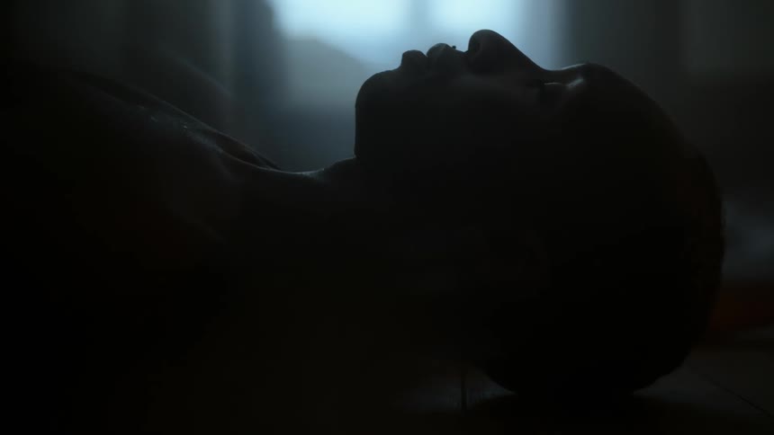 A man is lying on the floor breathing heavily as light shines in the window
