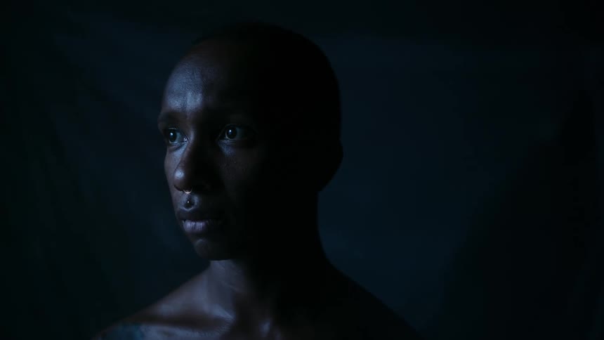 Light shines on the face of a man in a dark room looking very sad