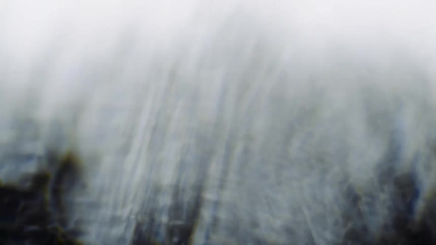 Light shines on a hazy textured smokey substance as it moves across the darkness