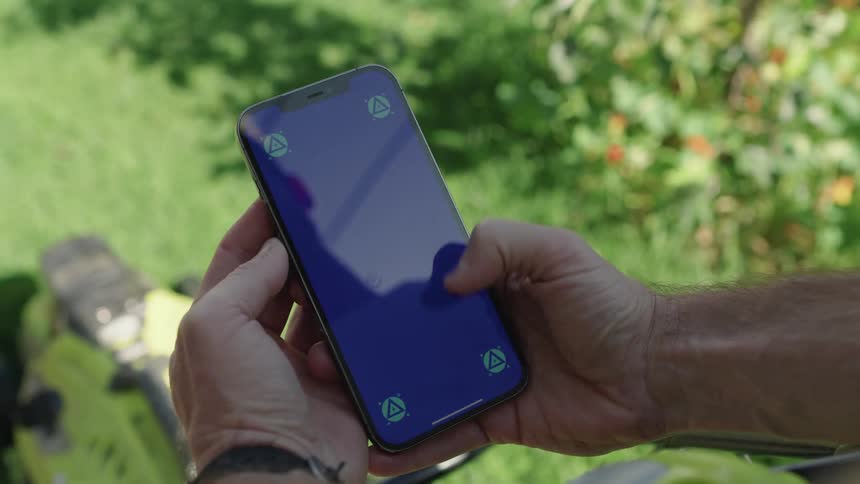 A persons fingers scrolling on their phone with green vegetation in the background