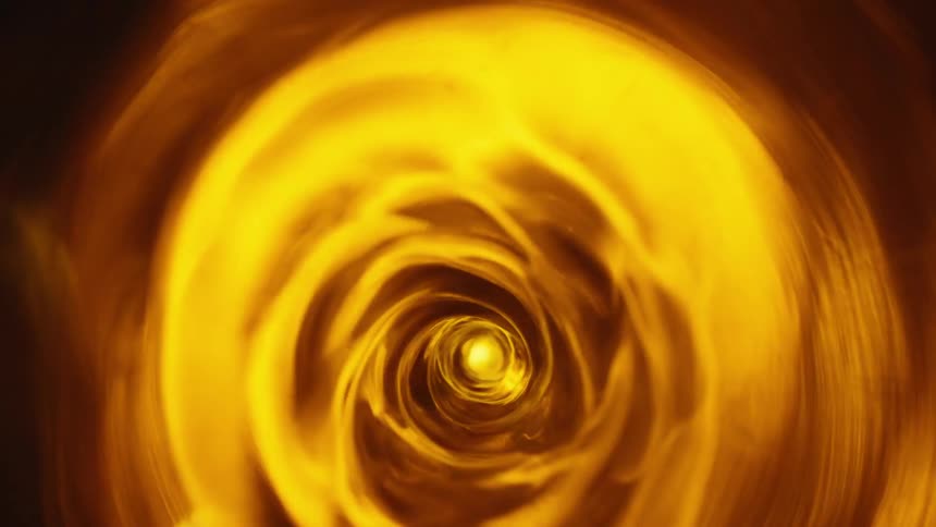 Amber fluid spins forming a vortex lit intermittently by light