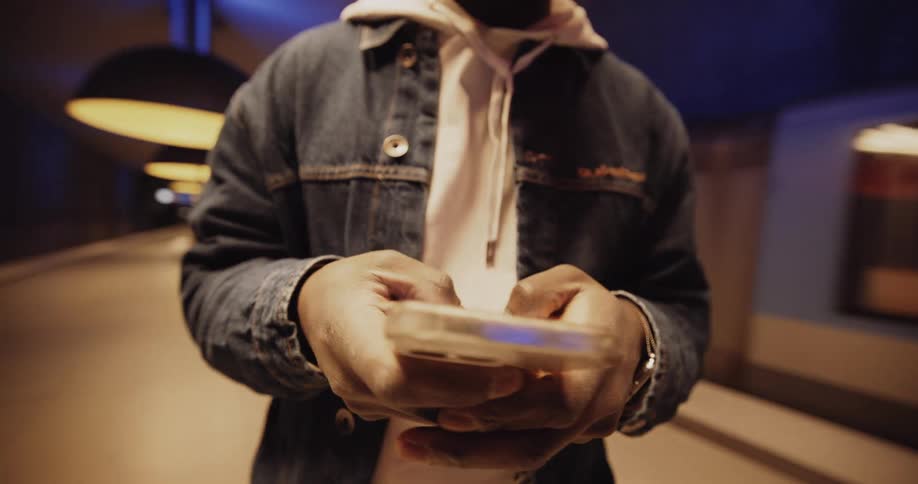 A person texting on their cell phone wearing a jean jacket while a subway goes by in the background