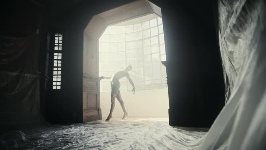 A male dancer moving his arms around while standing in a sunlit doorway