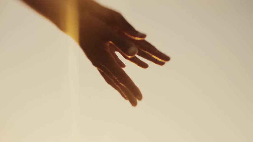 Close up of hands waving together in front of the sun at evening