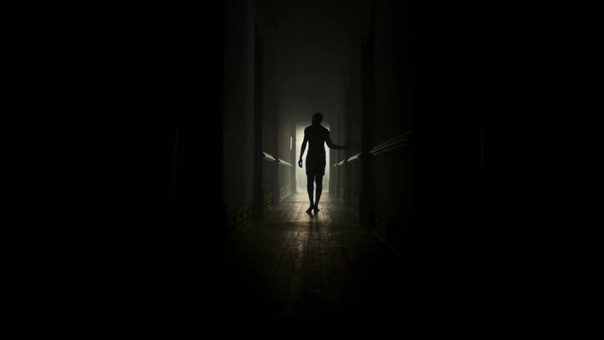 A man walks down the long dark hall