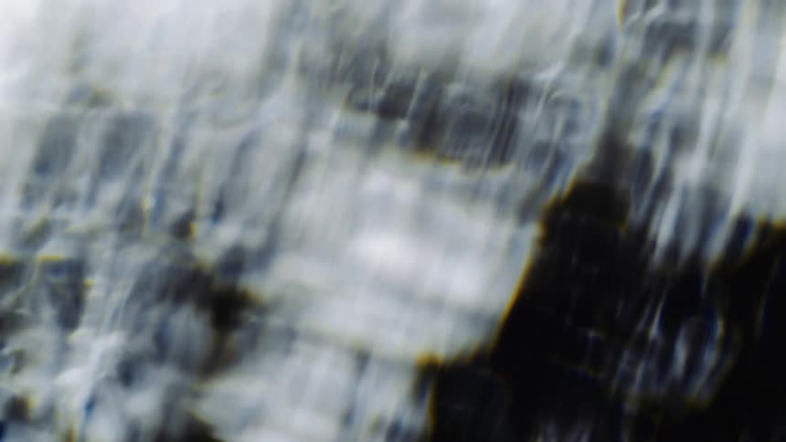 Blurry out of focus footage of the silhouette of shapes behind a waving water like screen