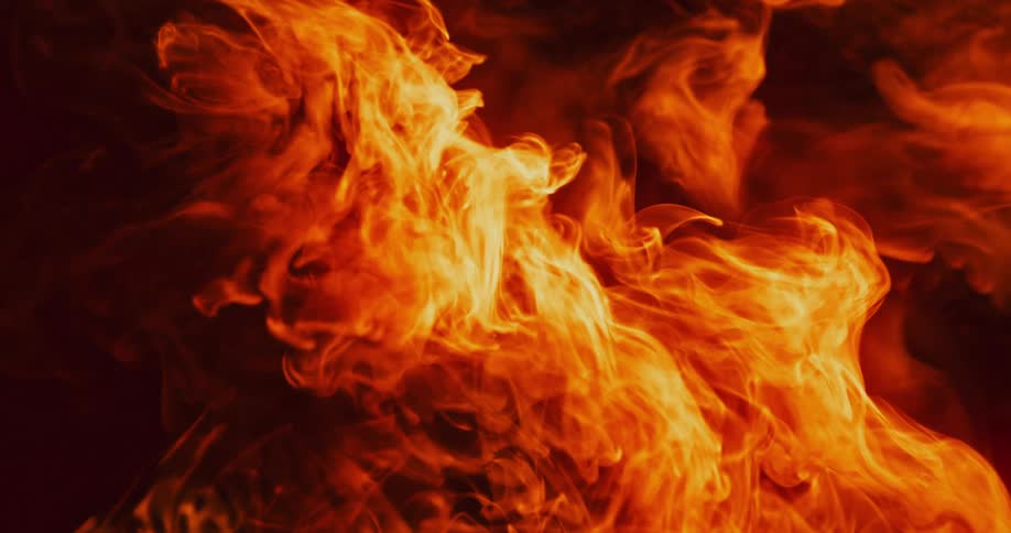 Slow motion footage of bright yellow flames slowly moving against a dark background