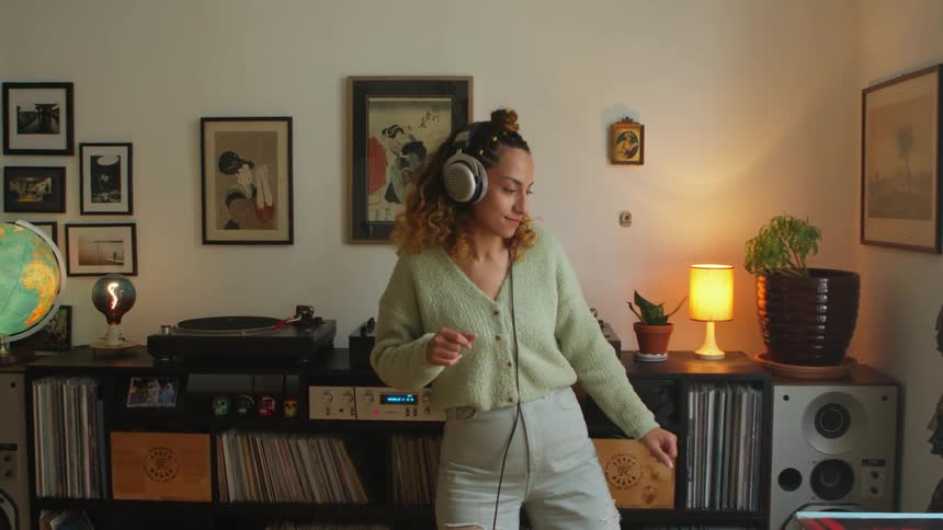 Woman dances while wearing headphones in room with several records and a record player