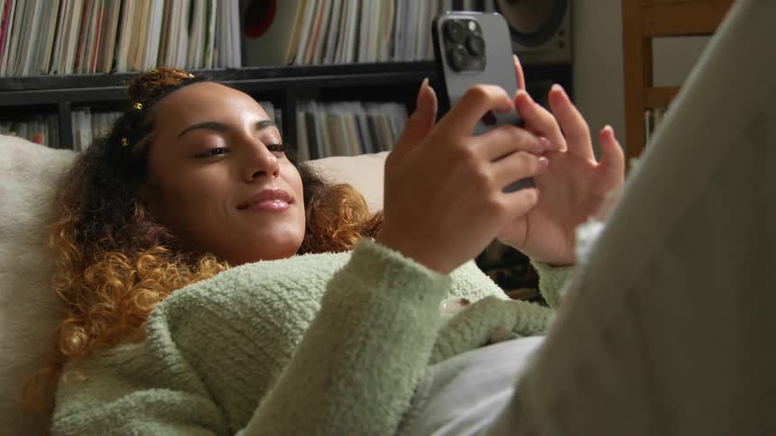 A woman smiling while relaxing and using her smartphone at home
