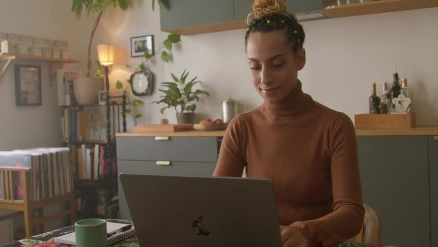 A young woman uses a laptop while sitting at a table indoors during the day