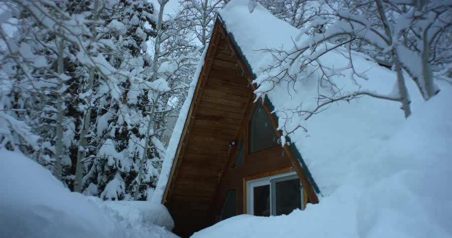 A thick blanket of snow covers an a frame cabin in the woods