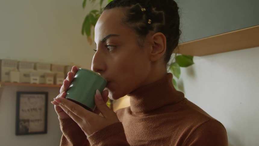A woman is holding a cup of hot coffee under her nose as steam rises she takes a sip