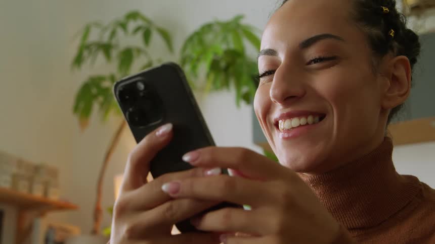 A woman is holding her phone with both hands with a smile on her face as she looks at it