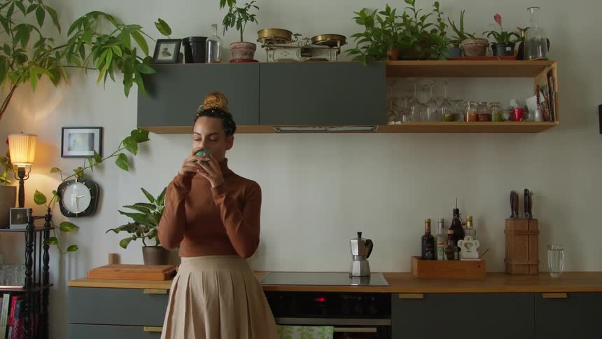 A woman drinks coffee while standing next to her stove