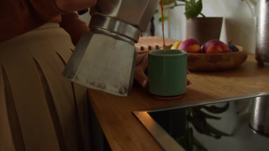 A woman picks up a silver metal teapot and pours herself a cup of hot tea