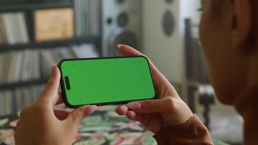 A woman is standing in her living room holding a phone with a green screen