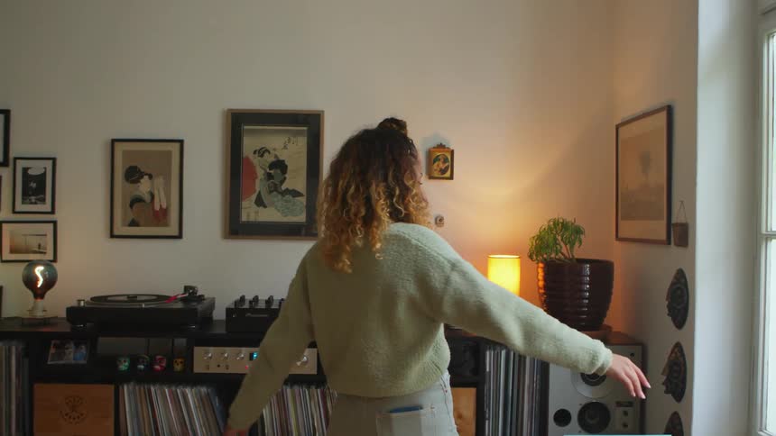 A woman dancing and spinning next to a record player at home