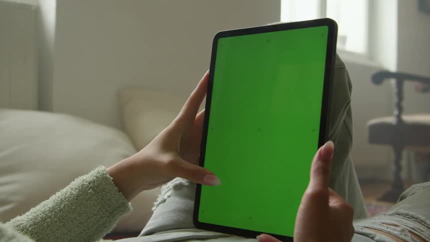 Woman wearing sweater scrolls on tablet while lying down