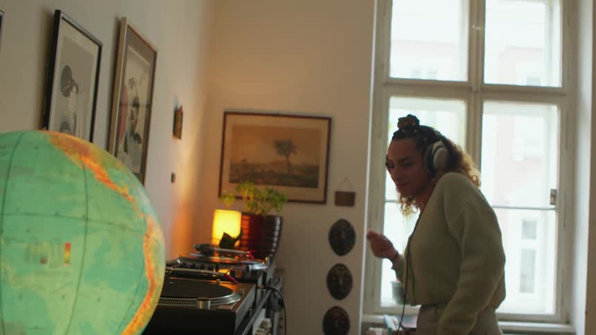 A woman wearing headphones is dancing in front of her stereo as a world globe is lit up on the table