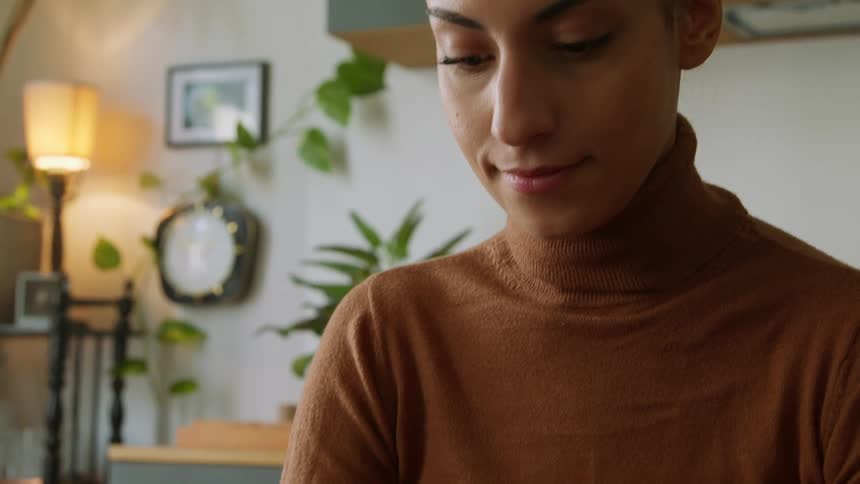 A woman at home smiles as she looks at her cell phone