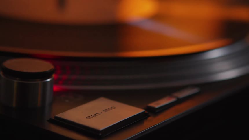 A woman pushes a button to start her turntable and puts the needle on a vinyl record
