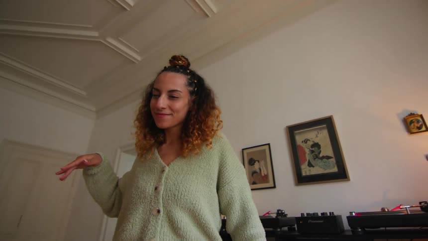 A woman is standing in her living room dancing in front of her turntable and record collection