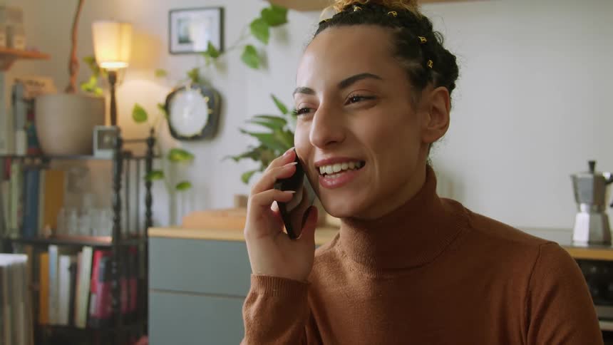A woman is smiling and laughing as she talks on her phone