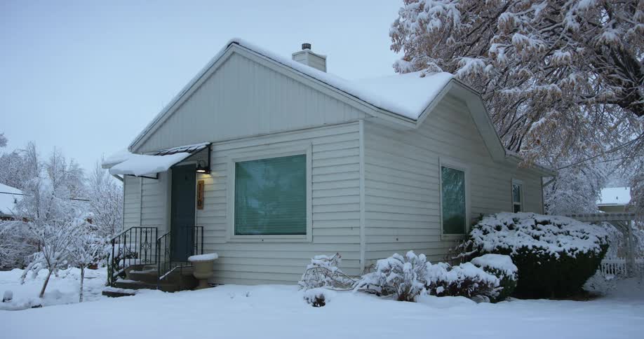 The porch light on a house is on in a snow covered neighborhood on a winter day