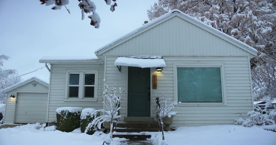 Wind blows a snow covered branch hanging over a home
