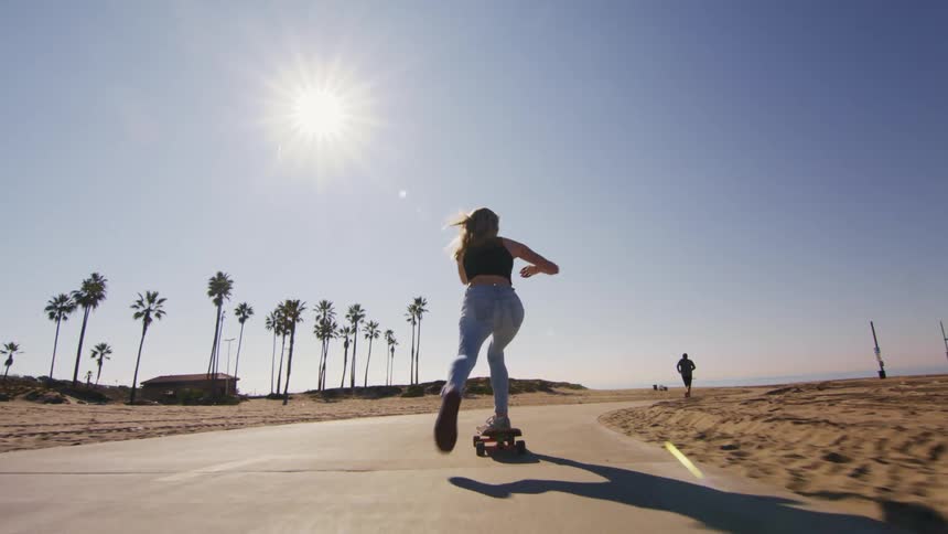 Woman skateboards along road coming up behind jogger on same road