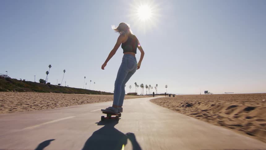 A teenage girl is riding a skateboard on a road through the beach
