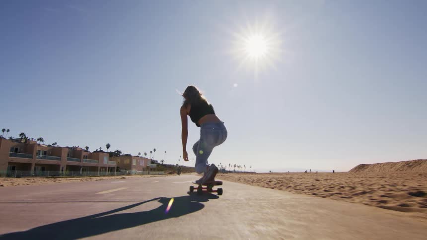 A woman skateboards down a trail running through the beach