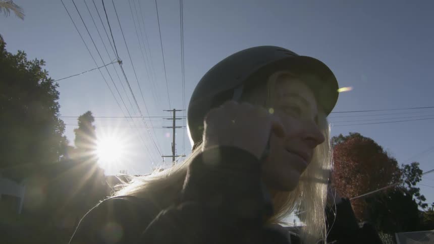 A woman smiling while putting on a helmet outside on a sunny day
