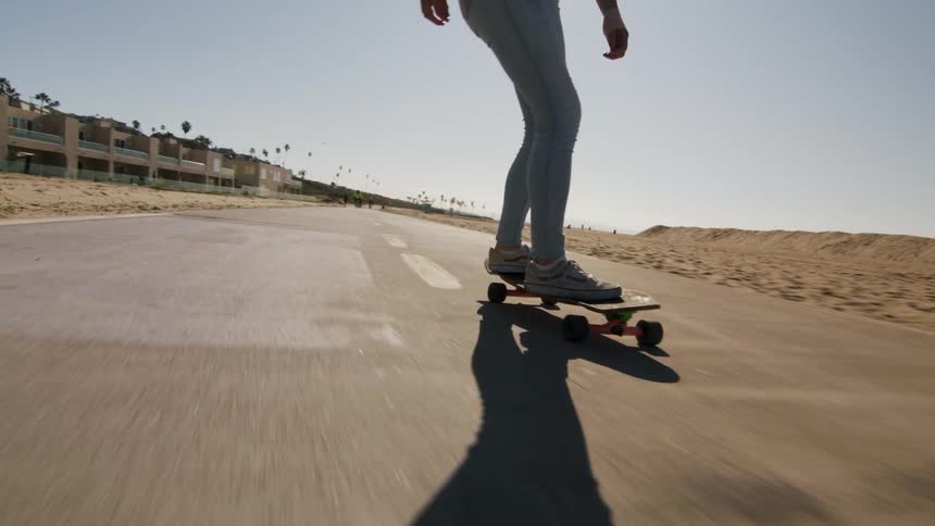 A woman skateboarding down a road in the middle of the day with the sun at her back
