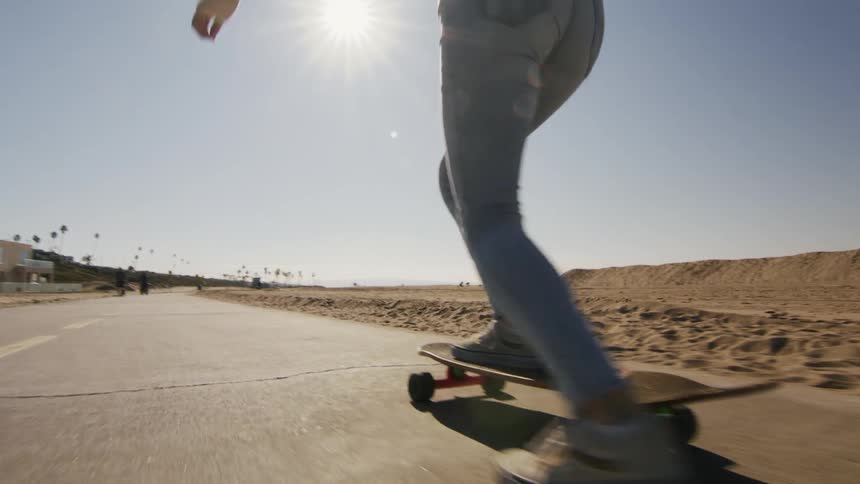 Woman with black top and jeans skateboards near the beach