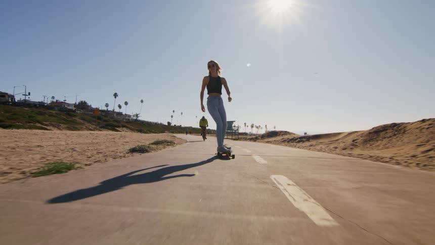 Young fit woman rides a skateboard on a road on a beach at daytime