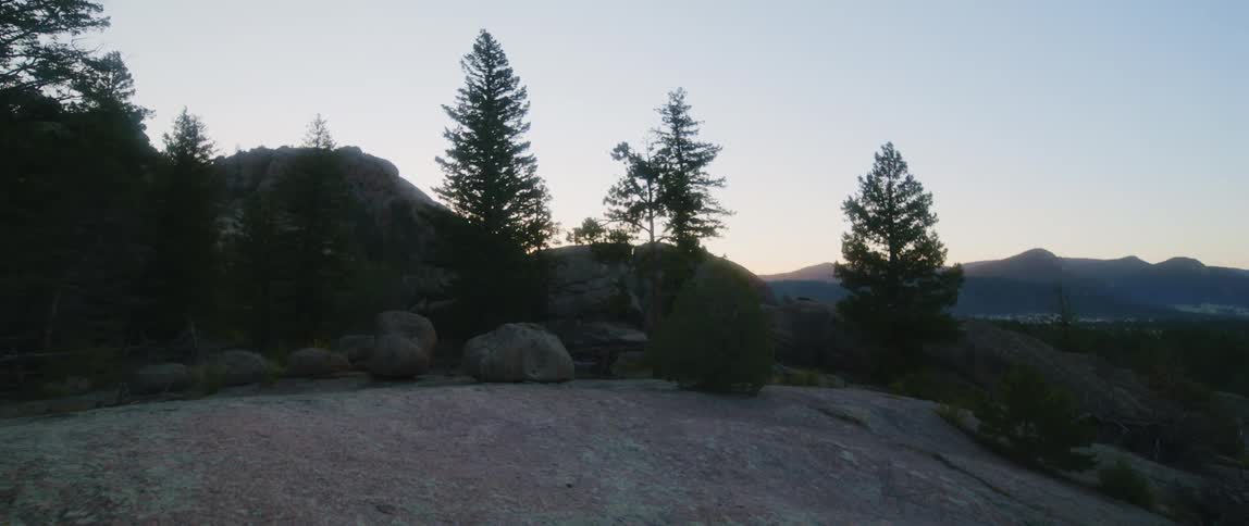 Boulders and trees are on top of a mountain and there are mountains in the distance