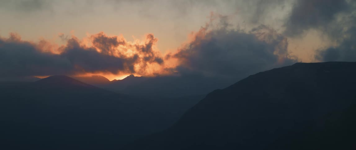 Landscape of sun going down behind clouds and mountains