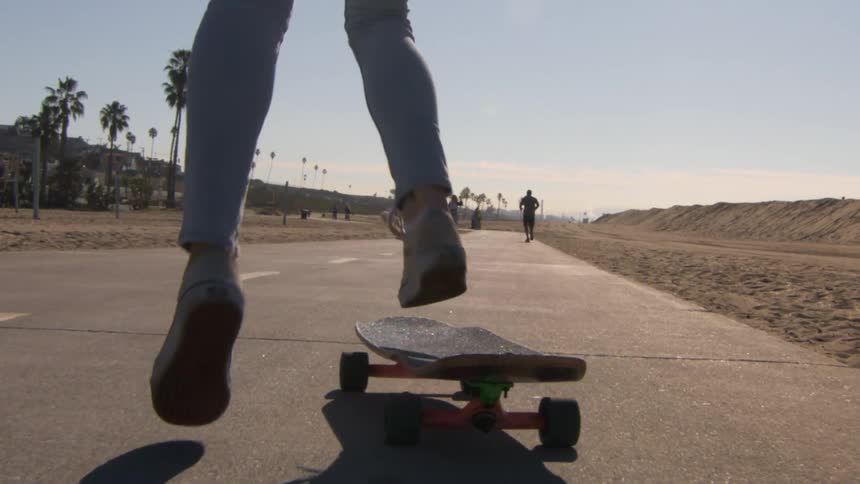 A persons feet jumping onto a skateboard rolling down a concrete roadway