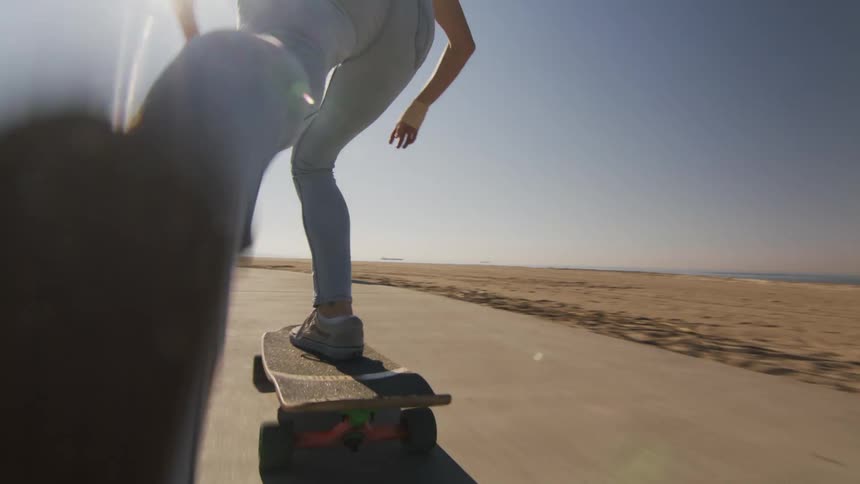 A woman rides her skateboard down a boardwalk on the beach
