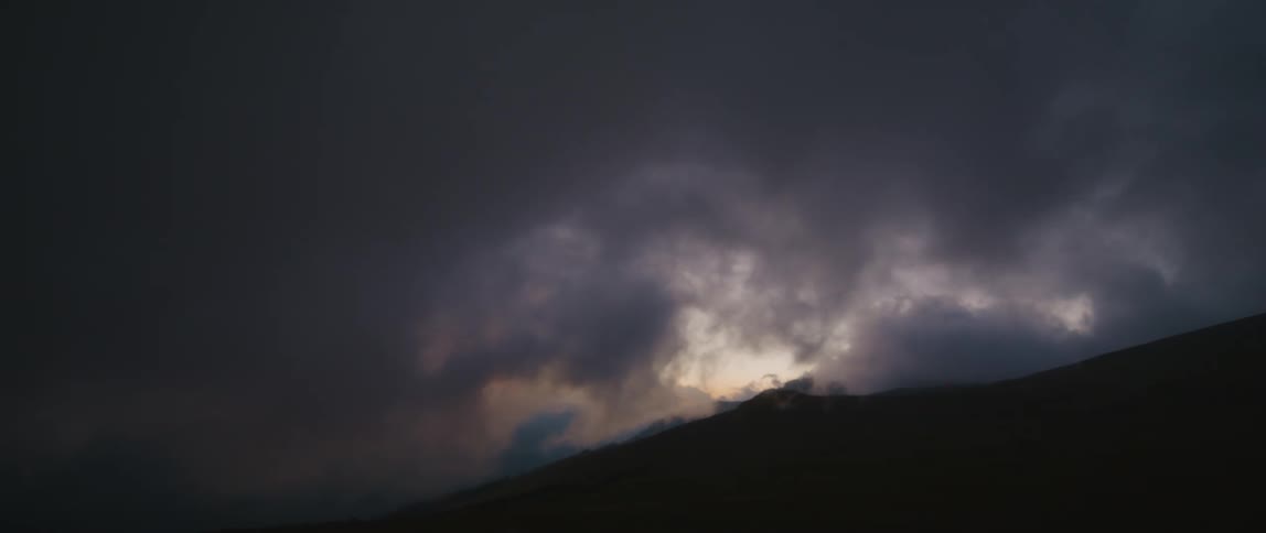 Dark storm clouds move over a mountain covering the bright daylight sky