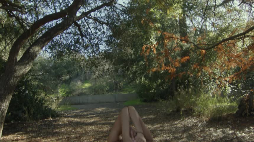 A woman doing yoga pulling her feet to her head in a forest under tall trees