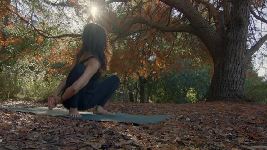Woman with wavy hair black top and leggings stretches on yoga mat in the autumn forest