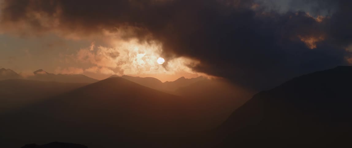 Sunlight shining through dense fog turns sky and silhouetted mountains red