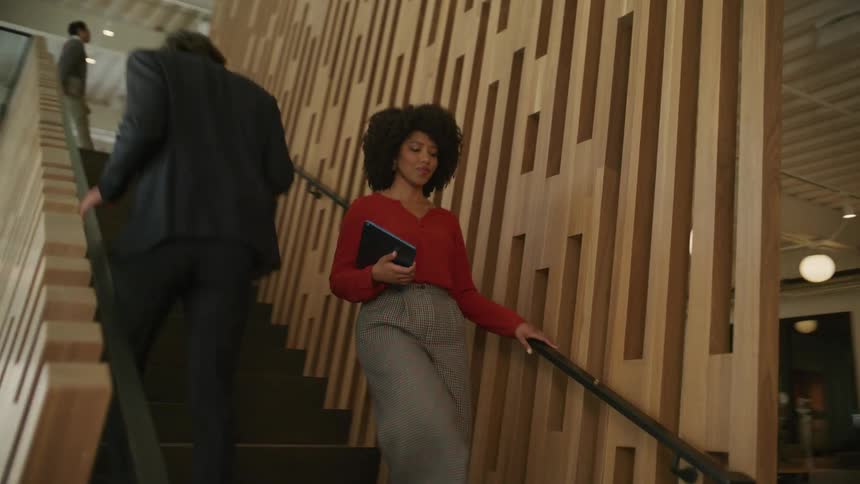 A woman is carrying a tablet computer as she walks down the stairs in an office building
